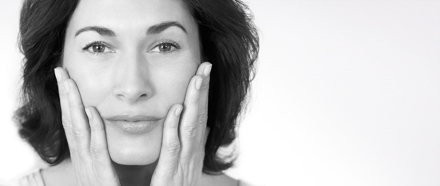 Una mujer de mediana edad tocándose las mejillas con ambas manos.