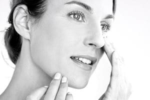 Una mujer aplicándose crema en la mejilla derecha.