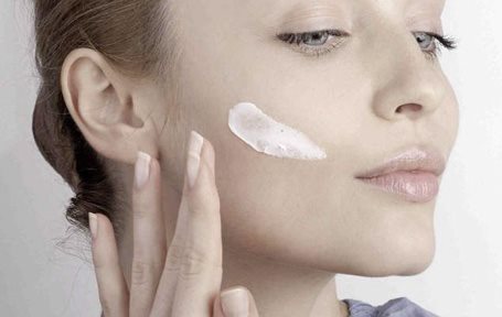 Mujer aplicándose crema en la mejilla